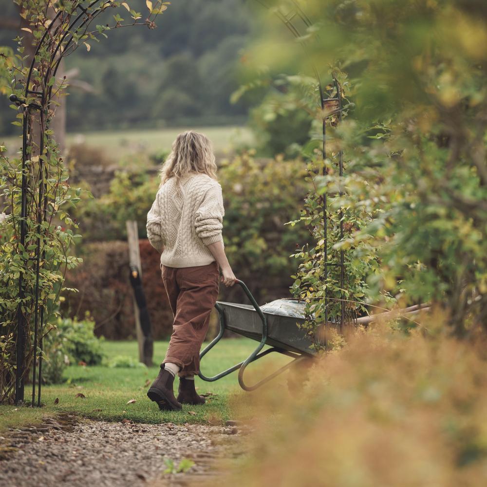 Woman in a garden setting walking with a wheelbarrow of gardening tools