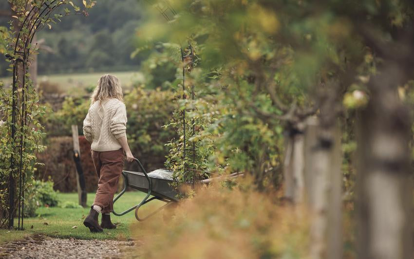 Woman in a garden setting wheeling a wheelbarrow of gardening tools